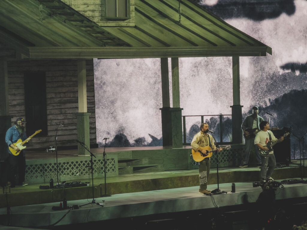 Noah Kahan and band performing on the porch of the cabin stage set