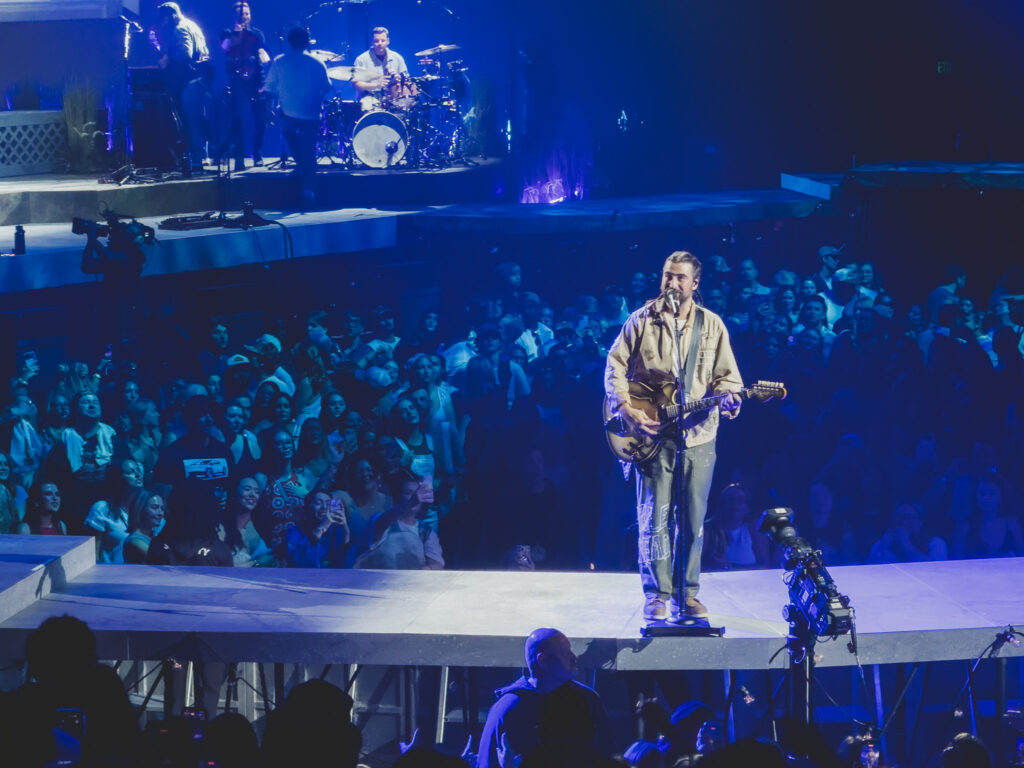 Noah Kahan singing on the runway stage in blue light, The Great Divide Tour