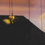 Noah Kahan performing We Go Way Back from the roof of the house set at sunset projection