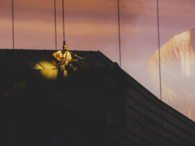 Noah Kahan performing We Go Way Back from the roof of the house set at sunset projection