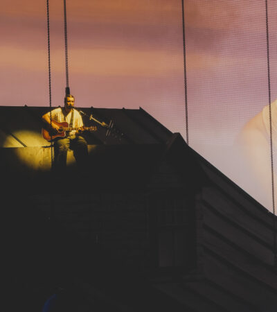 Noah Kahan performing We Go Way Back from the roof of the house set at sunset projection