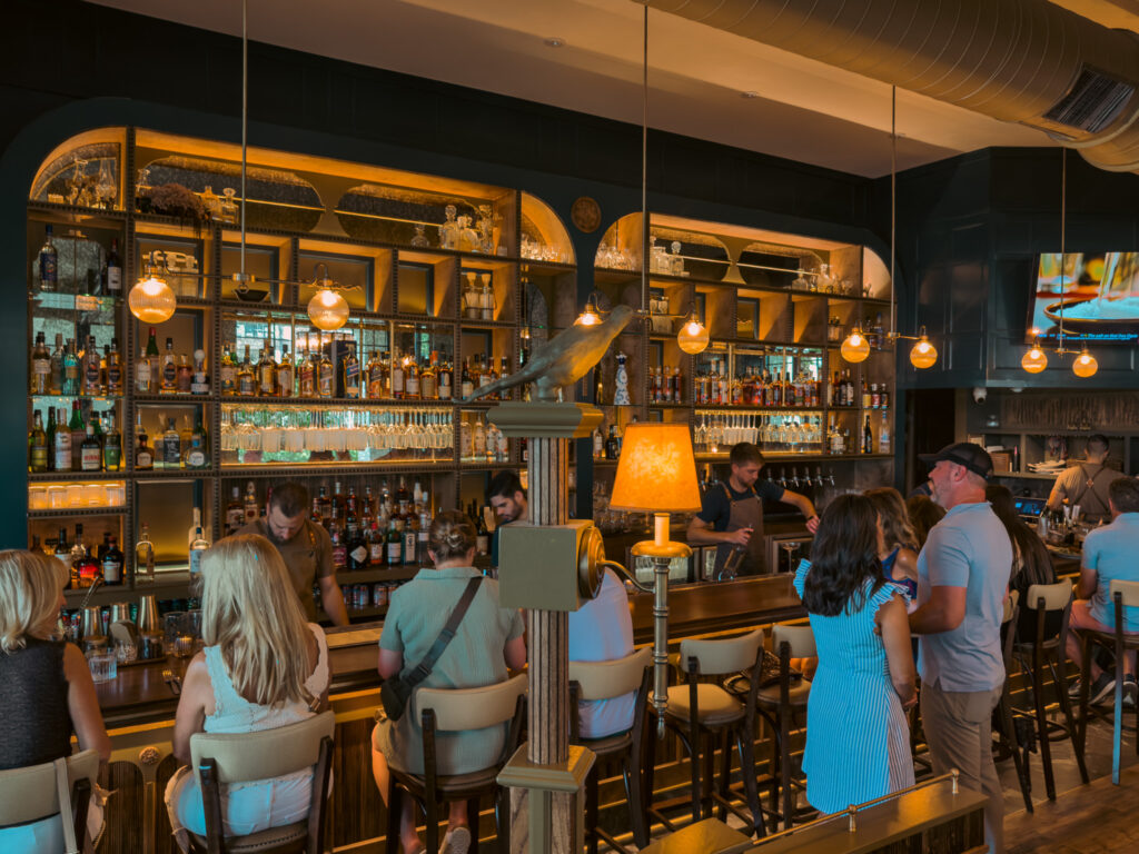Allswell - Waterside Place Review 87 Bartenders working behind the bar at Allswell at Waterside Place beneath globe pendant lights and arched mirrored shelving