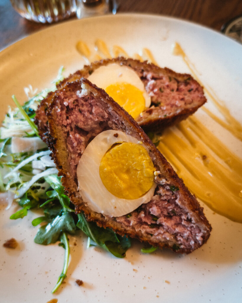 Allswell - Waterside Place Review 74 Scotch egg at Allswell cut open to show Berkshire pork sausage around a hard cooked egg, with greens and English mustard aioli