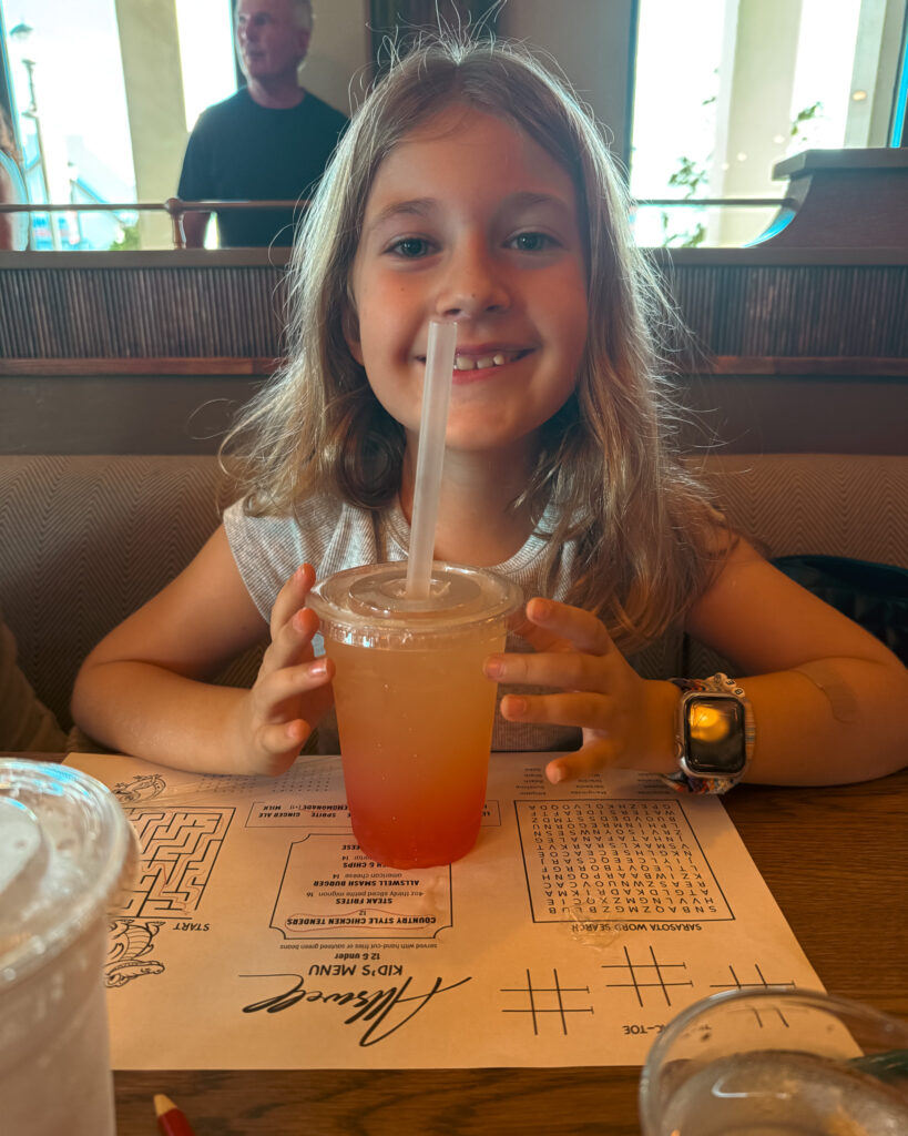 Allswell - Waterside Place Review 72 A young diner smiling with a strawberry boba lemonade over the Allswell kids menu placemat with games
