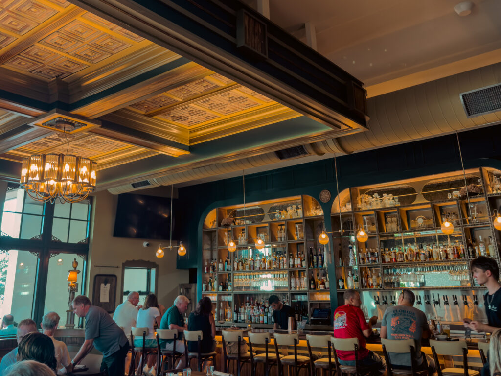 Allswell - Waterside Place Review 70 Wide view of the Allswell bar and dining room at Waterside Place showing the coffered ceiling, chandelier, and full bar
