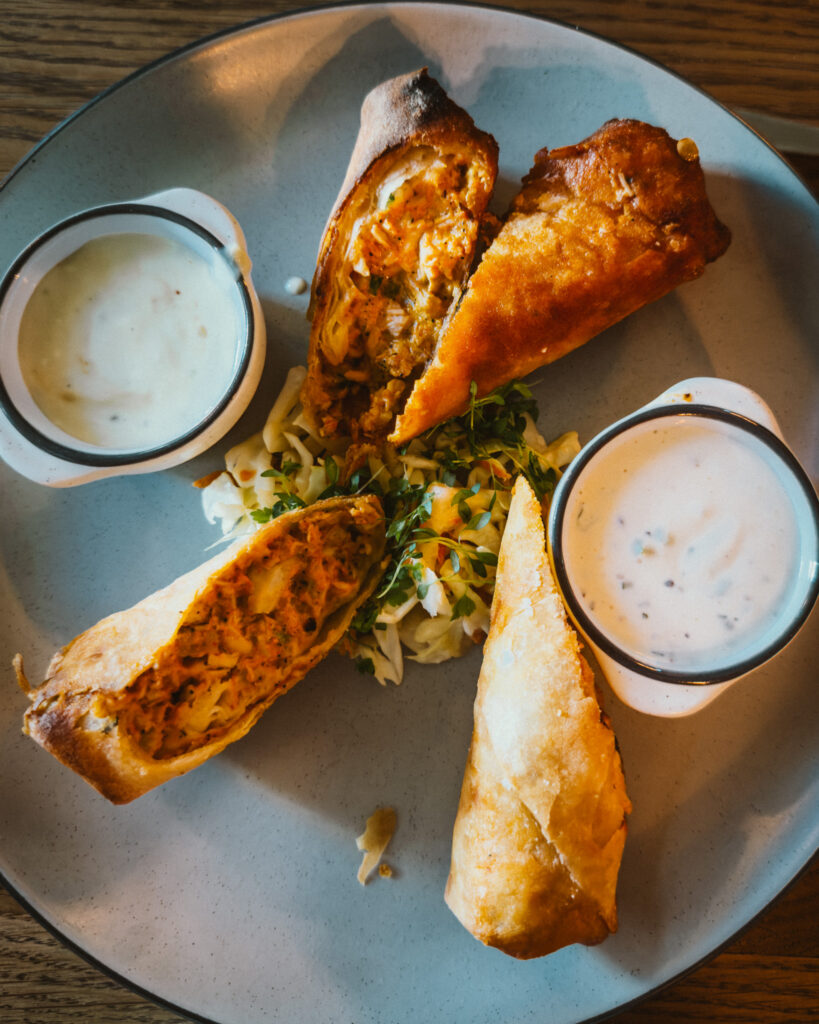 Allswell - Waterside Place Review 73 Buffalo chicken eggrolls at Allswell sliced open on a plate with slaw and two buffalo bleu dipping sauces